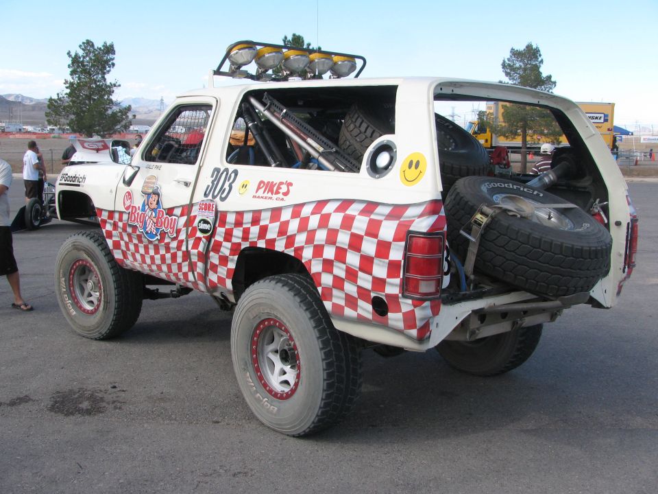 Rear three-quarter view of #303 checkered race truck with open tailgate and spare tires