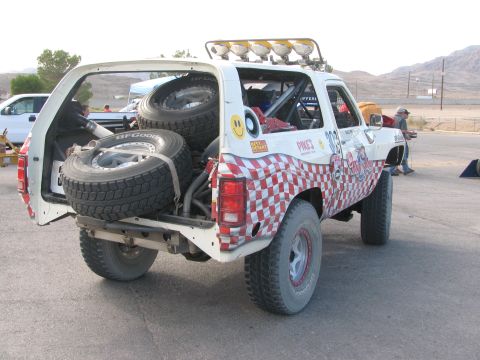 1990 Ford Bronco - 303 race truck photographed from behind with its rear hatch up, revealing stacked spare tires and the exposed chassis.