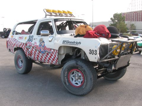1990 Ford Bronco - White number 303 desert race truck with Big Boy checkered graphics and a five-pod roof light bar parked in a lot.