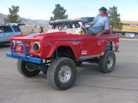 1990 Ford Bronco - red early Ford Bronco built for off-road racing with blue tube bumpers and a man seated in the open cockpit.