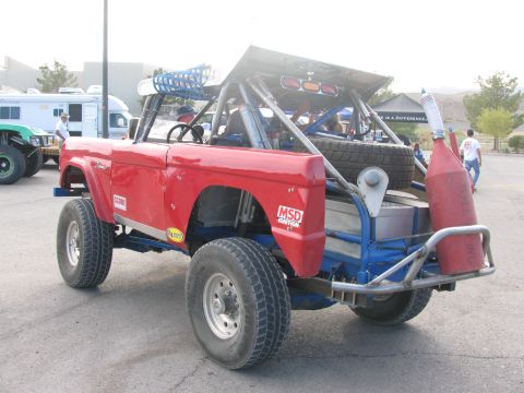 1990 Ford Bronco - Rear quarter of the red Bronco off-road racer showing its roll cage, rear-mounted spare tire and a fuel jug.