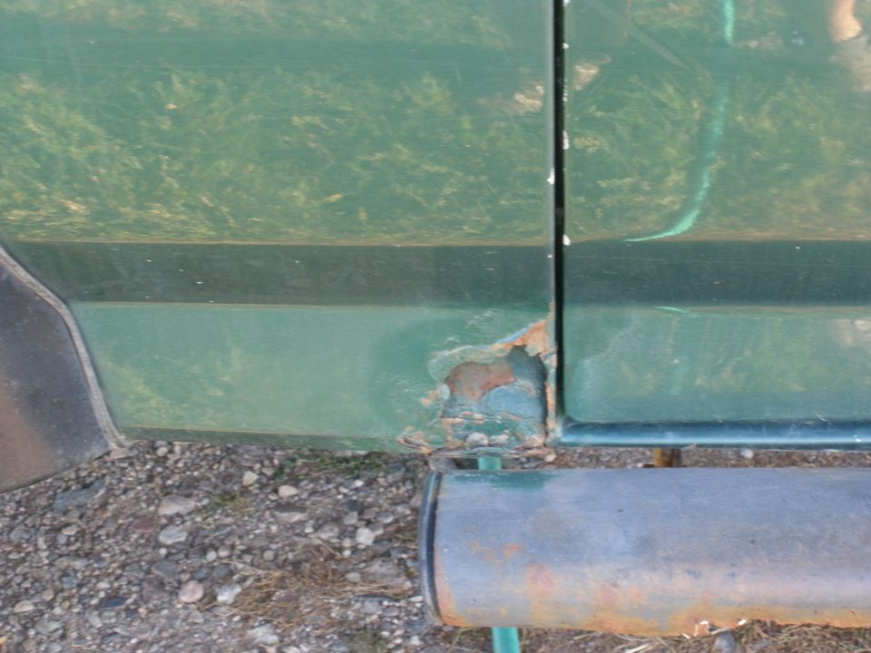 Green vehicle lower body panel with rust damage near the seam and a running board below