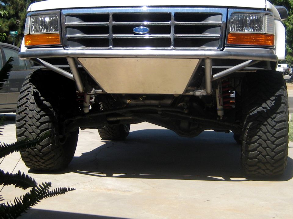 Front of a white Ford truck with a custom bumper and large tires. Grille has a blue Ford oval emblem