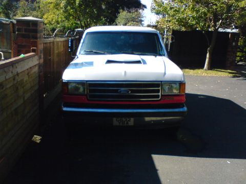 1989 Ford Bronco - This Ford Bronco is parked in a driveway with a wooden fence and trees in the background.