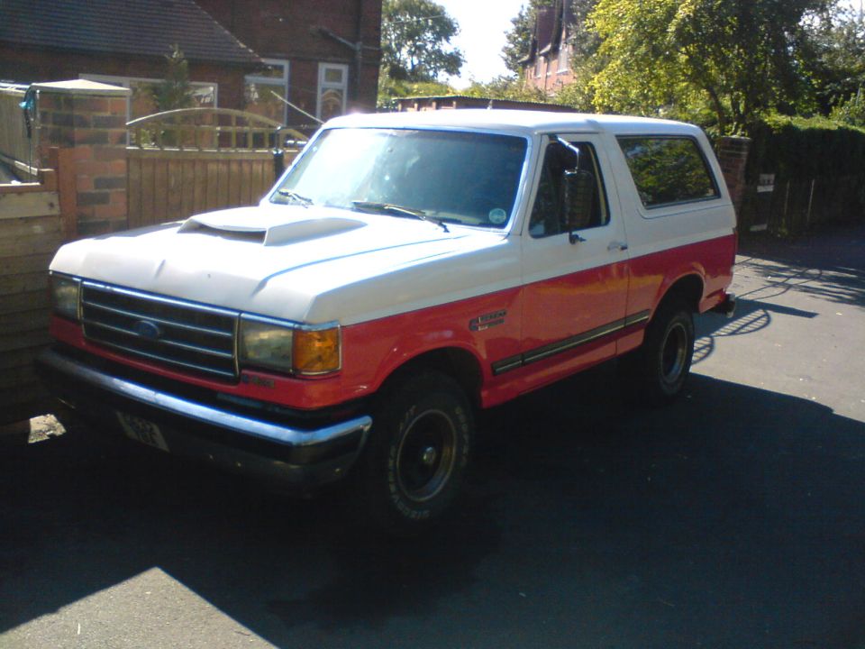 Two-tone white and red Ford Bronco with a hood scoop parked on a paved surface