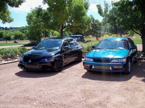 1972 Ford Ranchero - Two sedans, one black and one teal, are parked on a gravel lot under trees.