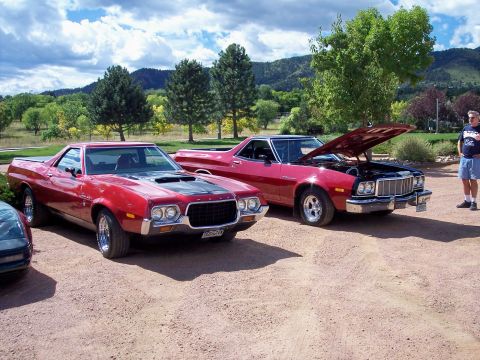 1972 Ford Ranchero - Two red Ford Rancheros are parked on a gravel lot with trees and hills in the background.