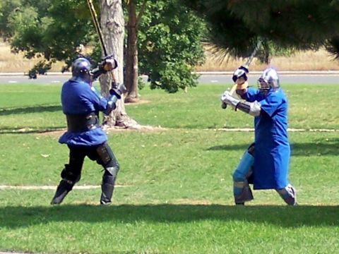 1972 Ford Ranchero - Two individuals engaged in a sword fight, dressed in protective armor and helmets, practice their combat skills outdoors.