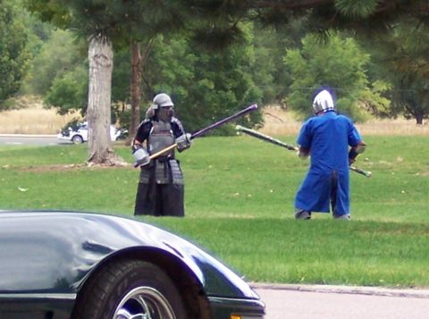 1972 Ford Ranchero - Two individuals in samurai armor engage in a mock battle on a grassy field, with a dark green car partially visible in the foreground.