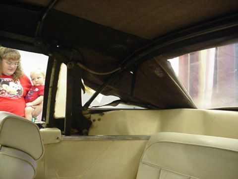 1977 Ford Mustang II - The interior of a convertible shows beige seats and the top mechanism, with a woman and child present.