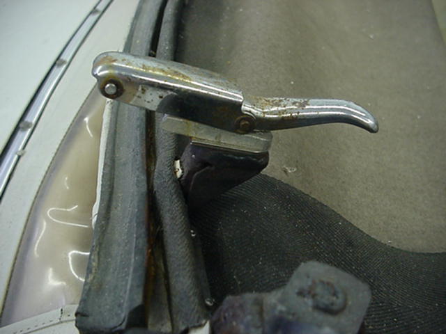 Chrome door handle mechanism with rust, attached to a black fabric interior and white exterior trim