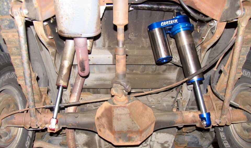 Underside view of a vehicle's rear axle with two blue Pro-Tech shocks and exhaust system