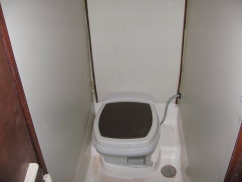 1990 Ford Bronco - portable cassette toilet with a closed lid sits in a cramped RV or trailer bathroom compartment.