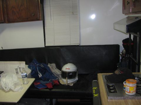1990 Ford Bronco - white full-face racing helmet rests on a dark vinyl bench seat in a cluttered trailer interior beside a water bottle and gear.