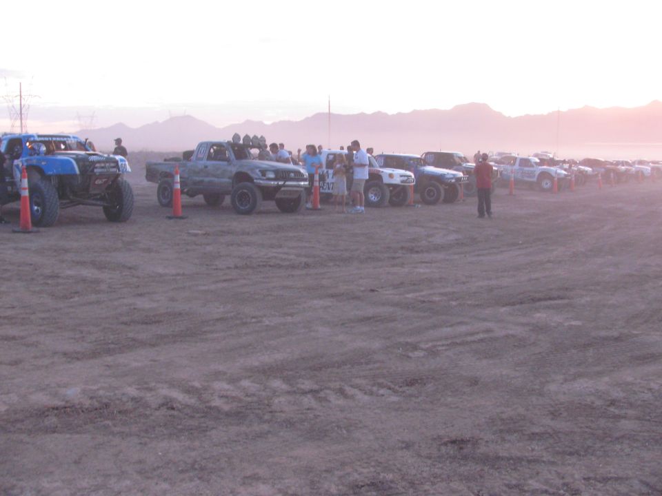 Row of off-road race trucks and buggies staged on a dusty desert lot at dawn