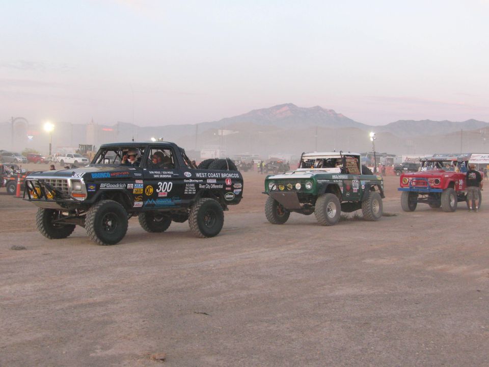 Black race pickup number 300 and other off-road vehicles lined up in the desert at dusk