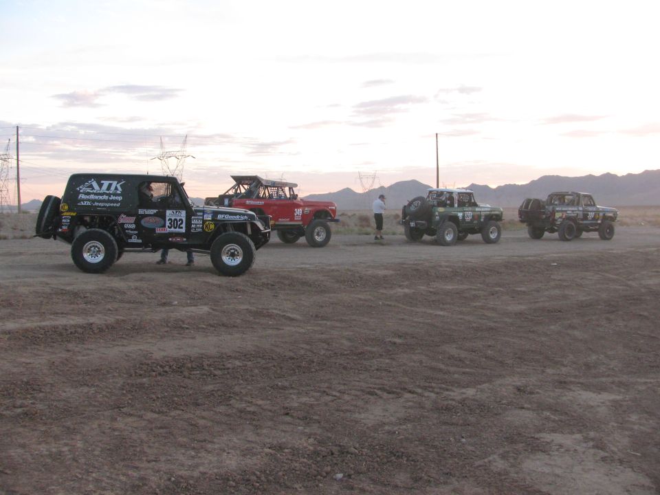 Black race Jeep number 302 leading a line of off-road vehicles on a desert flat