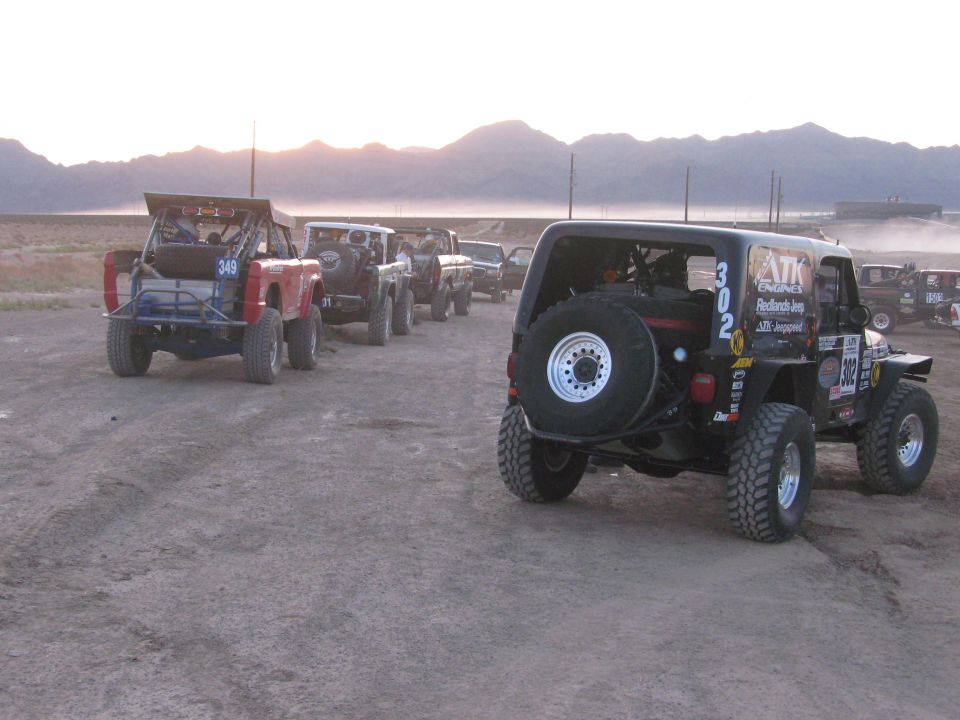 Rear view of black race Jeep number 302 with spare tire in a line of off-road vehicles