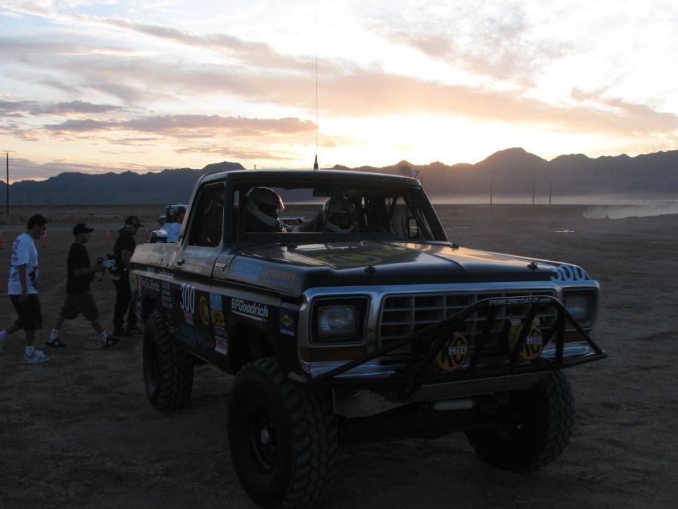 Black off-road race pickup number 300 staged at sunset with people standing nearby