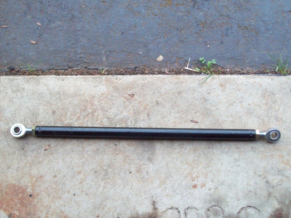 Black adjustable linkage rod with silver ends, lying on concrete and asphalt