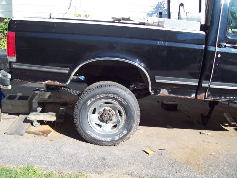 1989 Ford F-150 - Rear side view of a black 1989 Ford F-150 pickup truck with visible rust and suspension components for repair.