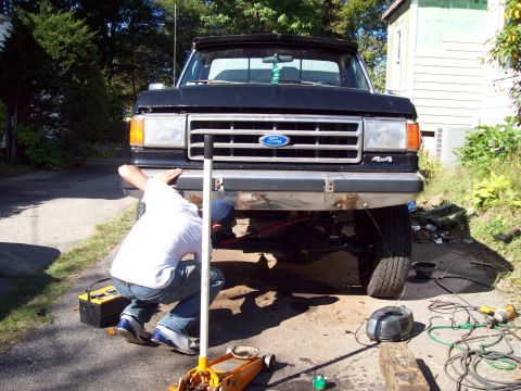 1989 Ford F-150 - A person is working on the front end of a black Ford F-150 pickup truck, with tools scattered around.