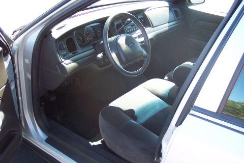 2001 Ford Crown Victoria - The interior of a 2001 Ford Crown Victoria, its dashboard, steering wheel, and front seats, is visible through the open driver's side door.