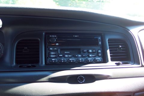 2001 Ford Crown Victoria - The dashboard of a car features a radio with AM/FM, CD, and tape functions, along with climate control vents.