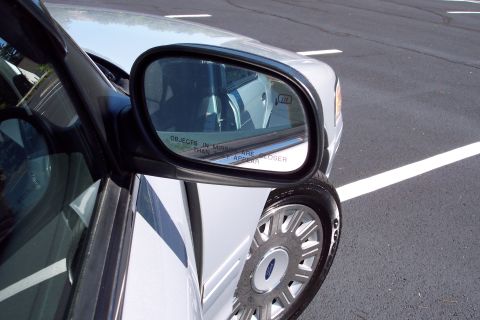 2001 Ford Crown Victoria - Close-up of the side mirror and wheel of a white 2001 Ford Crown Victoria, showing the Ford badge.
