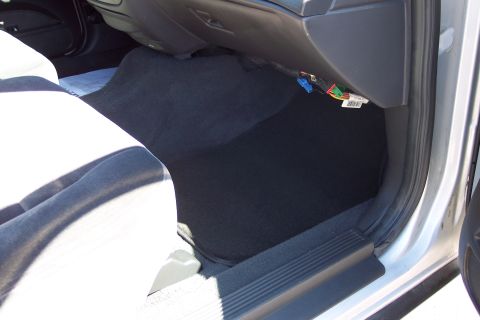 2001 Ford Crown Victoria - The interior of a car shows exposed wiring and black carpeting on the floor.