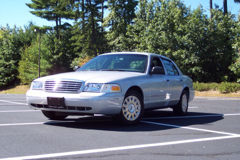 2001 Ford Crown Victoria - A silver 2001 Ford Crown Victoria is parked in an empty lot with trees in the background.