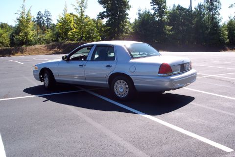 2001 Ford Crown Victoria - A silver sedan is parked in an empty lot under a clear sky.