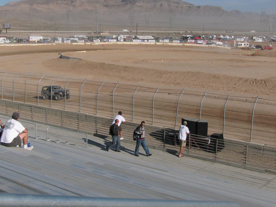 Tube-frame off-road racer on dirt track as fans walk the grandstand