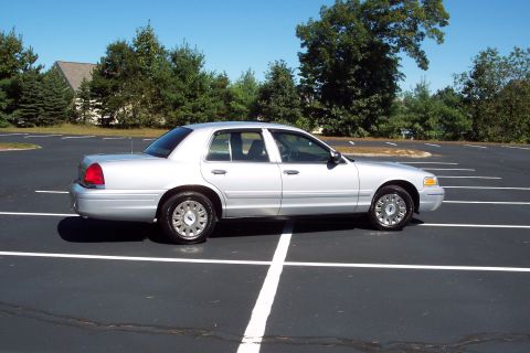 2001 Ford Crown Victoria - A silver sedan is parked in an empty lot on a clear day.