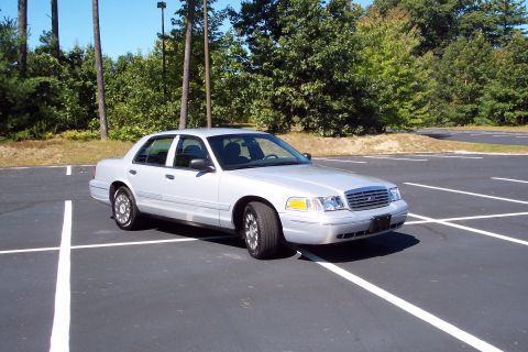 2001 Ford Crown Victoria - A silver 2001 Ford Crown Victoria is parked in a lot with trees in the background.