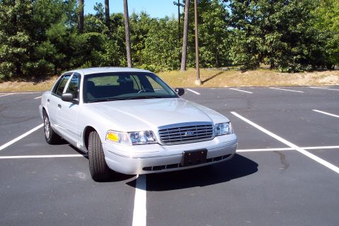 2001 Ford Crown Victoria - This silver sedan, likely a 2003 model based on its grille and headlights, is parked in an empty lot.