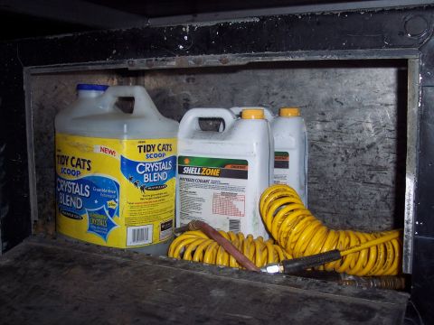 1981 Kenworth W900A - Contents of a storage compartment include Tidy Cats litter, Shell Zone antifreeze, and a yellow air hose with fittings.