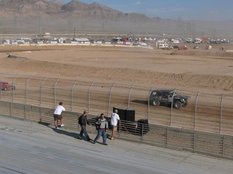 1990 Ford Bronco - Two off-road racers, one red and one dark, run a desert dirt oval as spectators watch from the grandstand rail.