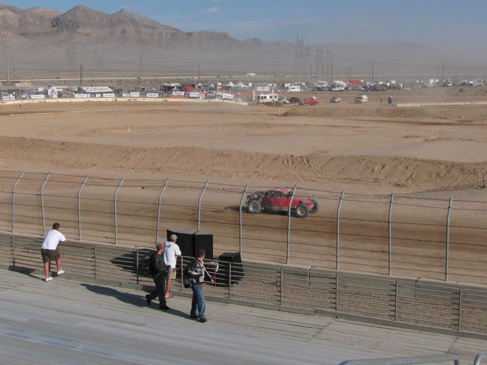 Red off-road racer on desert dirt oval viewed from grandstand