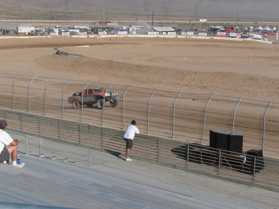 Orange off-road race truck on desert dirt oval with spectators