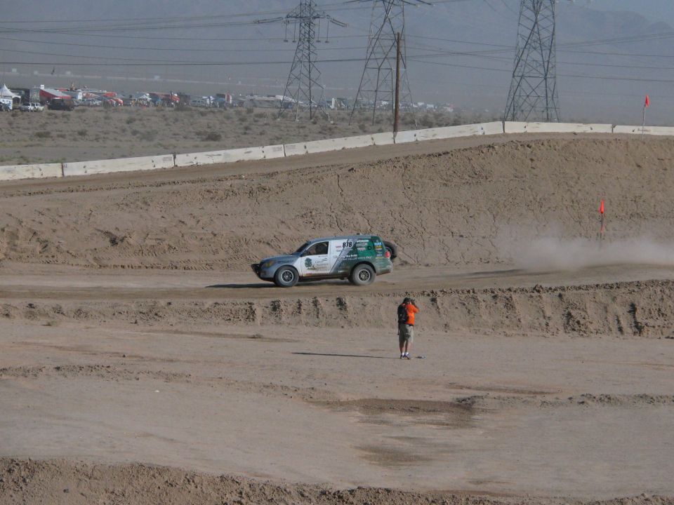 Silver and green off-road racer on dirt course with flagger and pylons