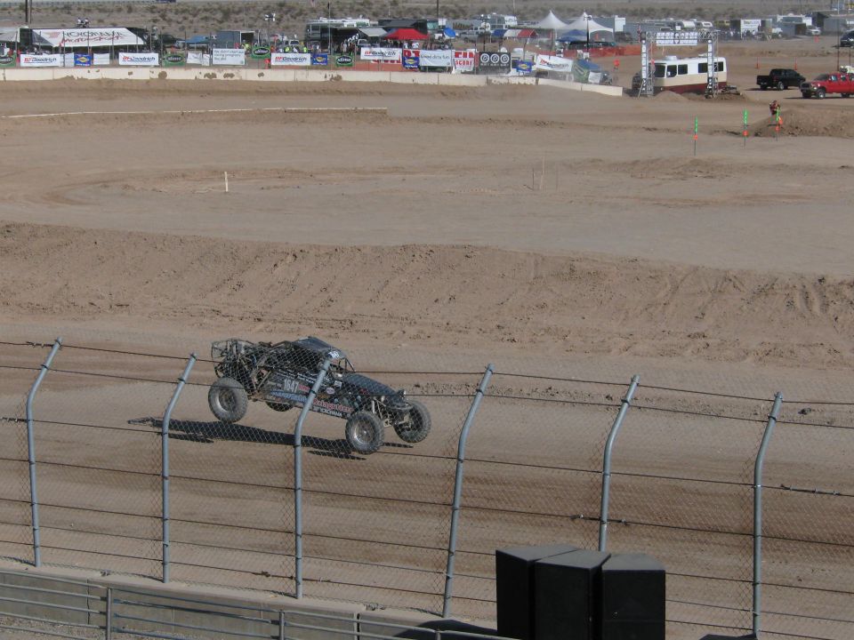 Dark tube-frame off-road race truck rounding a dirt oval track