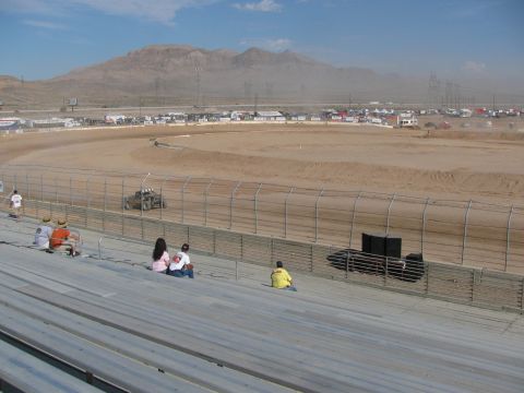 1990 Ford Bronco - Spectators sit on metal grandstand bleachers overlooking a dirt oval racetrack with desert mountains in the distance.