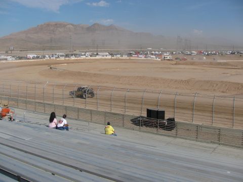 1990 Ford Bronco - lone off-road race truck runs the dirt track below grandstand seating with arid mountains on the horizon.