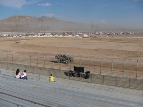 1990 Ford Bronco - off-road race truck travels along the dirt oval course with a hazy desert mountain range in the background.