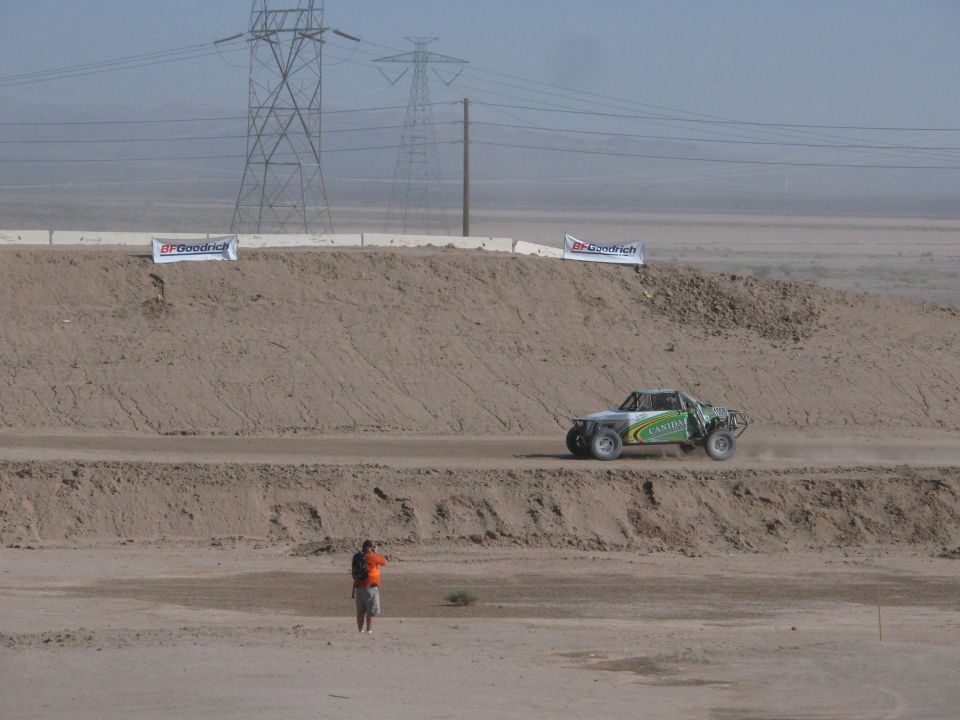 Green off-road race truck climbing dirt berm near power transmission towers