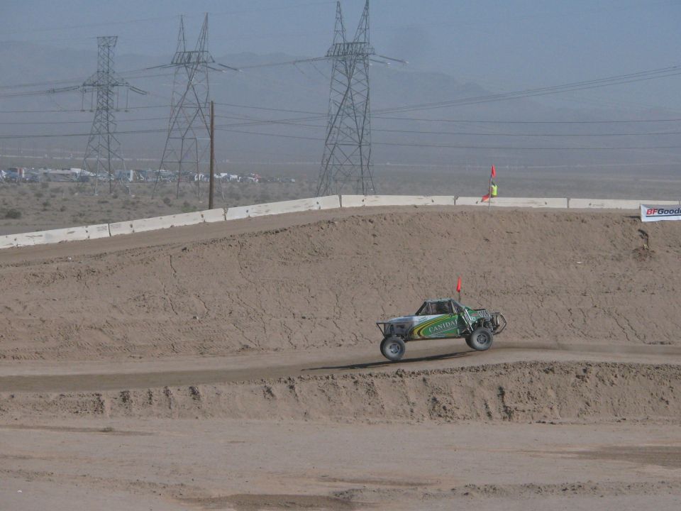 Green off-road race truck on dirt track below electrical transmission towers