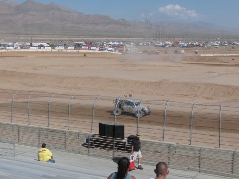 1990 Ford Bronco - off-road race truck kicks up a dust cloud rounding the dirt track as spectators look on from the grandstands.
