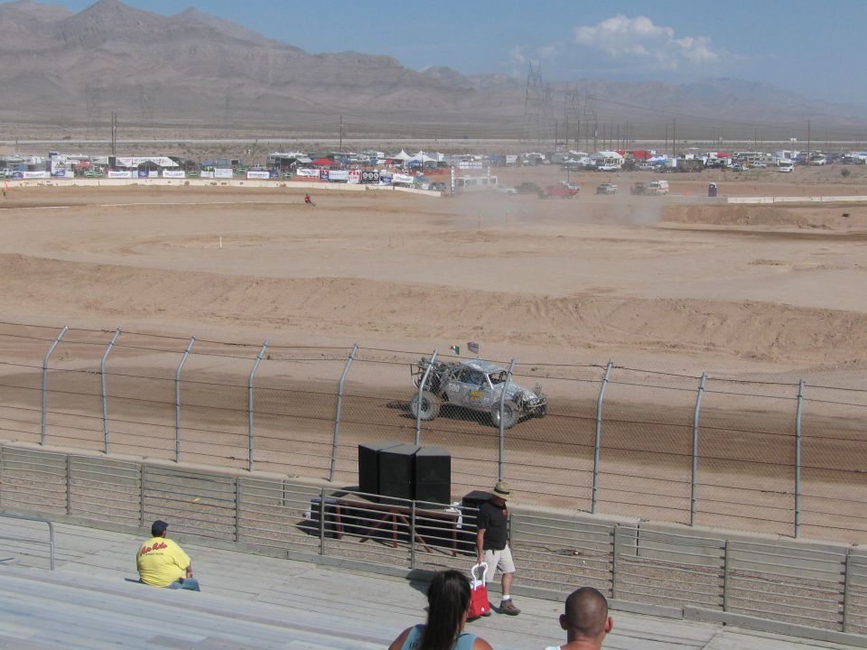 Off-road race truck kicking up dust on dirt track with spectators watching