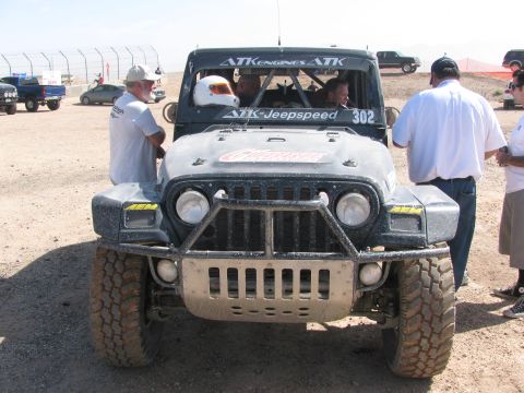 1990 Ford Bronco - Front view of a modified black Jeep race vehicle marked 302 in the pit area, with crew and spectators gathered around.